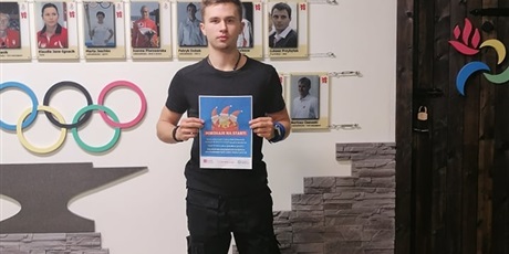 Powiększ grafikę: Hubert z plakatem na tle Kuźni Olimpijczyków w ZSSiMS