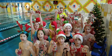 Powiększ grafikę: Klasa pływacka w strojach mikołajkowych pozuje do zdjęcia na basenie ZSSiMS.