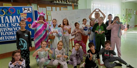 Powiększ grafikę: Panie trenerki wraz z uczniami przebranymi w piżamy pozują do zdjęcia na holu szkoły.