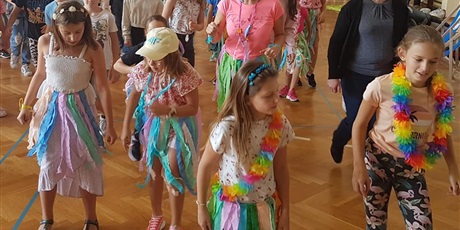 Powiększ grafikę: Kolorowo przebrane dzieci z klasy młodszych wraz z panią Wicedyrektor i trenerkami tańczą do muzyki Jerusalema na sali gimnastycznej.